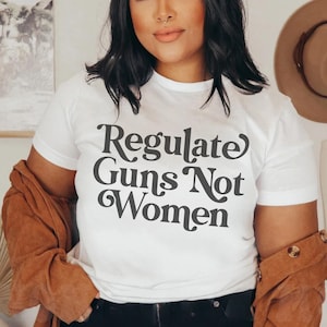 May include: White t-shirt with the text "Regulate Guns Not Women" in a retro font.
