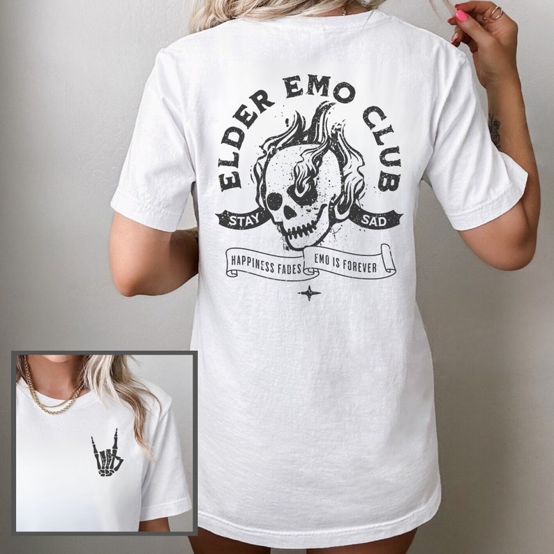 May include: White t-shirt with a black graphic print of a skull with flames on the back. The graphic says "Elder Emo Club" with the text "Stay Sad" above the skull and "Happiness Fades Emo is Forever" below the skull. The front of the shirt has a black graphic print of a skeleton hand making the rock and roll hand gesture.