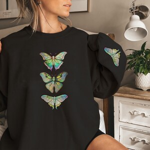 May include: Black sweatshirt with a vertical row of four iridescent butterfly graphics. The butterflies are in shades of green, blue, and purple.