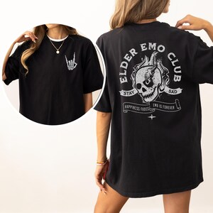May include: Black oversized t-shirt with a graphic print of a skull in flames and the text "Elder Emo Club". The text "Stay Sad" is above the skull and "Happiness Fades Emo is Forever" is below the skull.