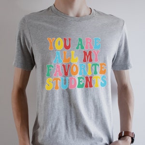 May include: A grey t-shirt with the text "You are all my favourite students" in colourful letters.