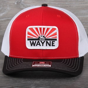 May include: Red, white, and black trucker hat with a white patch that says "WAYNE" and a graphic of a sunrise with a silhouette of a horse and rider. The hat is made by Richardson.