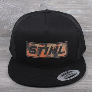 May include: Black trucker hat with a camouflage pattern 'STIHL' logo on the front. The hat has a black mesh back and a snap closure.