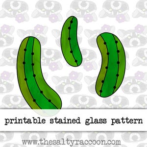 May include: A digital graphic featuring three green pickle shapes with black dotted lines down the center, set against a repeating raccoon pattern background. The text reads printable stained glass pattern and www.thesaltyraccoon.com.