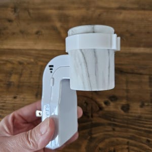 May include: White electric essential oil diffuser with a marble-patterned diffuser cup. The diffuser has a plug-in design and a button labelled "Timers".