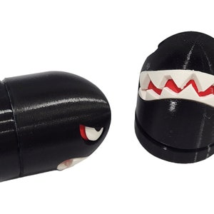 Puede incluir: Dos figuras negras impresas en 3D de un personaje de videojuego. Una figura es una vista lateral del personaje con un ojo rojo y dientes blancos. La otra figura es una vista frontal del personaje con una gran boca blanca con dientes rojos.