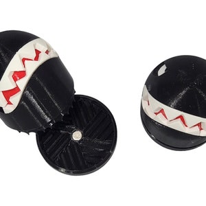 Puede incluir: Dos figuras impresas en 3D en blanco y negro de un personaje de videojuego con una sonrisa de dientes. Las figuras son de pl&aacute;stico y tienen una superficie texturizada.