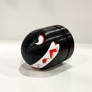 Puede incluir: Una figura impresa en 3D en blanco y negro de un Bill Bala de la serie de videojuegos Super Mario Bros. La figura tiene un ojo rojo y dientes afilados.