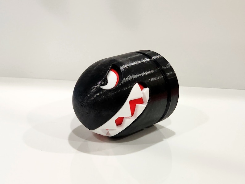 Puede incluir: Una figura impresa en 3D en blanco y negro de un Bill Bala de la serie de videojuegos Super Mario Bros. La figura tiene un ojo rojo y dientes afilados.