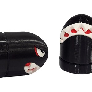 Puede incluir: Dos figuritas en forma de bala, impresas en 3D, en blanco y negro con dientes rojos. Las figuritas est&aacute;n inspiradas en un personaje de videojuego popular.