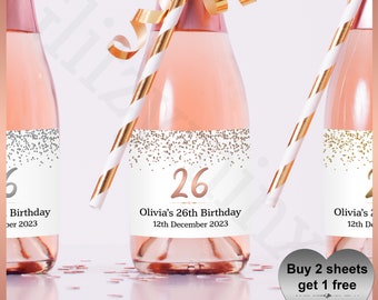 May include: A set of three mini champagne bottles with personalized labels for a 26th birthday. The labels feature a white background with gold and silver glitter confetti and the text "Olivia's 26th Birthday" and the date. The labels also include the number 26 in rose gold. A heart-shaped sticker with the text "Buy 2 sheets get 1 free Large & Small Labels" is in the lower right corner.
