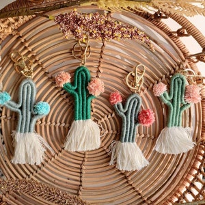 May include: Four colorful, handmade cactus keychains with pom-poms and tassels hanging on a woven wicker basket.