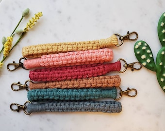 May include: A set of six colorful crocheted keychains with gold metal key rings. The keychains are in shades of yellow, pink, red, brown, teal, and gray.