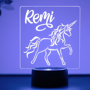 May include: A white acrylic night light with a unicorn silhouette and the name "Remi" in a cursive font. The light is on a black base.