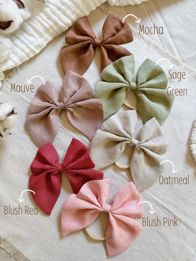 May include: Ten different colors of fabric hair bows, including blush pink, blush red, oatmeal, sage green, mauve, mocha. The bows are made of a soft, textured fabric and are tied with a knot in the center.