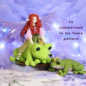 May include: A crocheted fairy doll with purple wings and a pink dress riding a green crocheted frog. The frog is wearing a gold crown. The fairy and frog are sitting on a wooden base. In the background, there is text that reads "In comparison to my faery pattern".