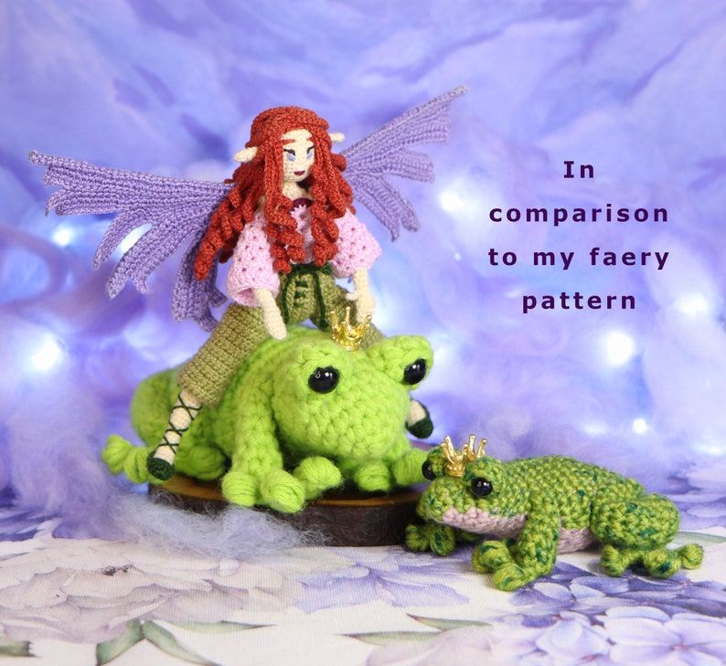 May include: A crocheted fairy doll with purple wings and a pink dress riding a green crocheted frog. The frog is wearing a gold crown. The fairy and frog are sitting on a wooden base. In the background, there is text that reads "In comparison to my faery pattern".