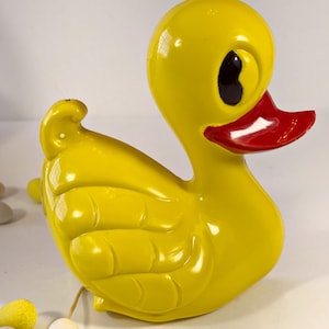 May include: A yellow rubber duck toy with a red beak and black eyes. The duck has a textured surface and is in a sitting position.