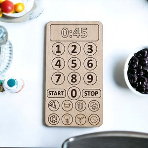 May include: A wooden kitchen timer with a digital display showing 0:45. The timer has a number pad with numbers 1 through 9, a start button, a stop button, and a zero button. There are also icons for pizza, coffee, popcorn, broccoli, a gear, a lightbulb, a fan, and a clock.