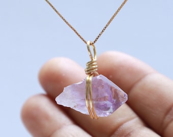 May include: A delicate gold chain necklace with a raw amethyst crystal pendant wrapped in gold wire.