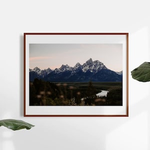May include: A framed photograph of a mountain range with snow-capped peaks, a river winding through a valley, and a forest in the foreground. The sky is a soft blue with a hint of pink.