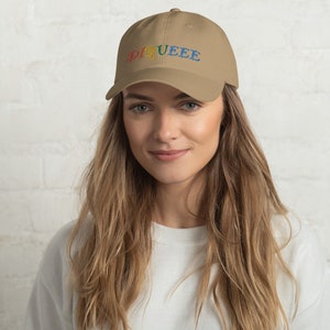 May include: A tan baseball cap with the word "DIQUEEE" embroidered in rainbow colours.