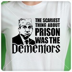 May include: A white t-shirt with a black and white graphic of a man with a hat and the text "The scariest thing about prison was the Dementors".