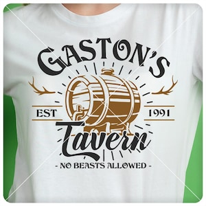 May include: White t-shirt featuring a brown and black graphic design. The design includes the words "Gaston's Tavern" above a brown barrel illustration, with "EST 1991" and "- NO BEASTS ALLOWED -" below.