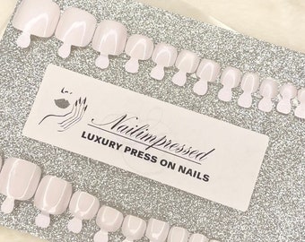 May include: A set of white press-on nails in various sizes, displayed on a silver glitter background. The card reads "Nailmpressed LUXURY PRESS ON NAILS".
