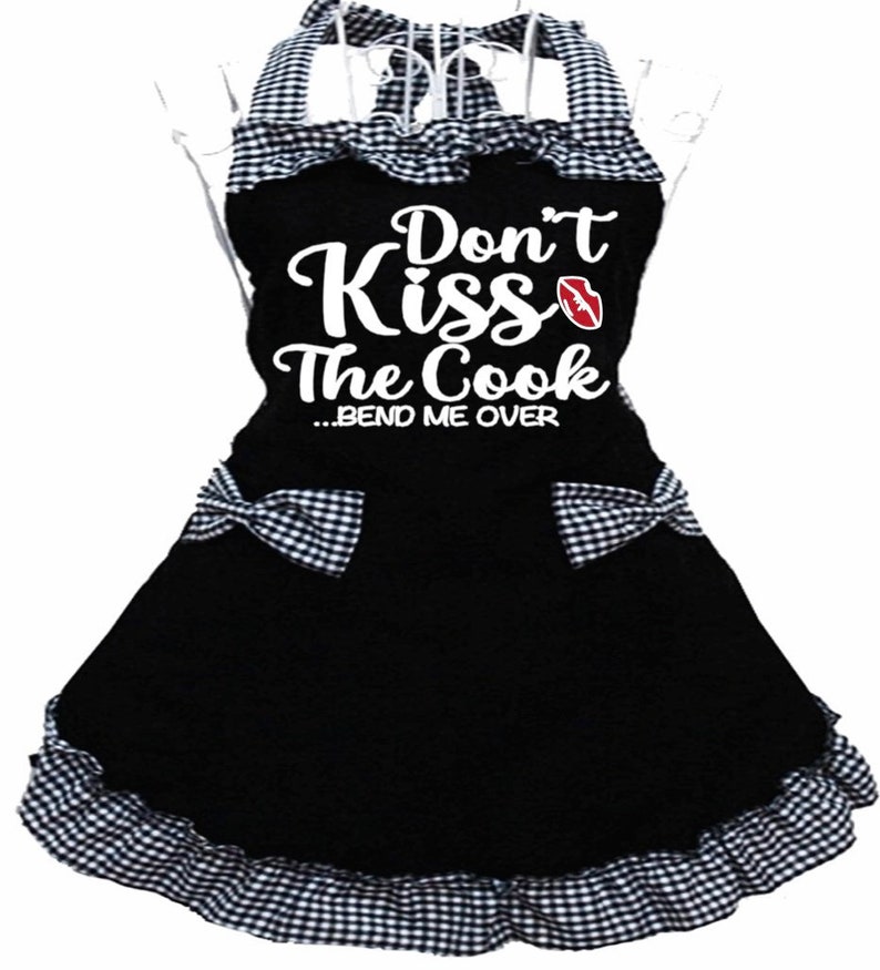 Puede incluir: Delantal a cuadros blanco y negro con un gr&aacute;fico blanco que dice "Don't Kiss The Cook...Bend Me Over" con una impresi&oacute;n de labios rojos.