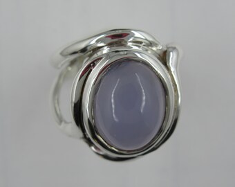 May include: A silver ring featuring a large, oval, lavender-colored gemstone. The ring has a smooth, polished band that curves around the stone, creating a modern and elegant design. The gemstone is the focal point.