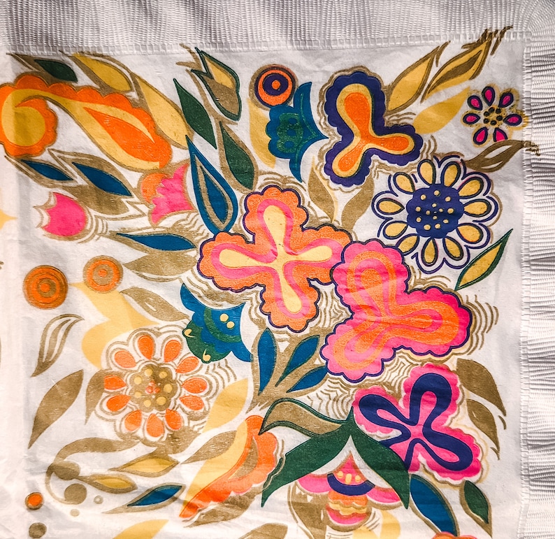 May include: A white fabric with a colorful floral pattern. The design features pink, yellow, orange, green, and blue flowers with intricate details. The background is white with a subtle texture.