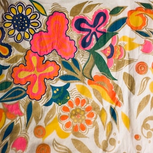 May include: A white fabric with a colorful floral pattern. The flowers are in shades of pink, orange, yellow, blue, and green. The fabric has a textured surface.