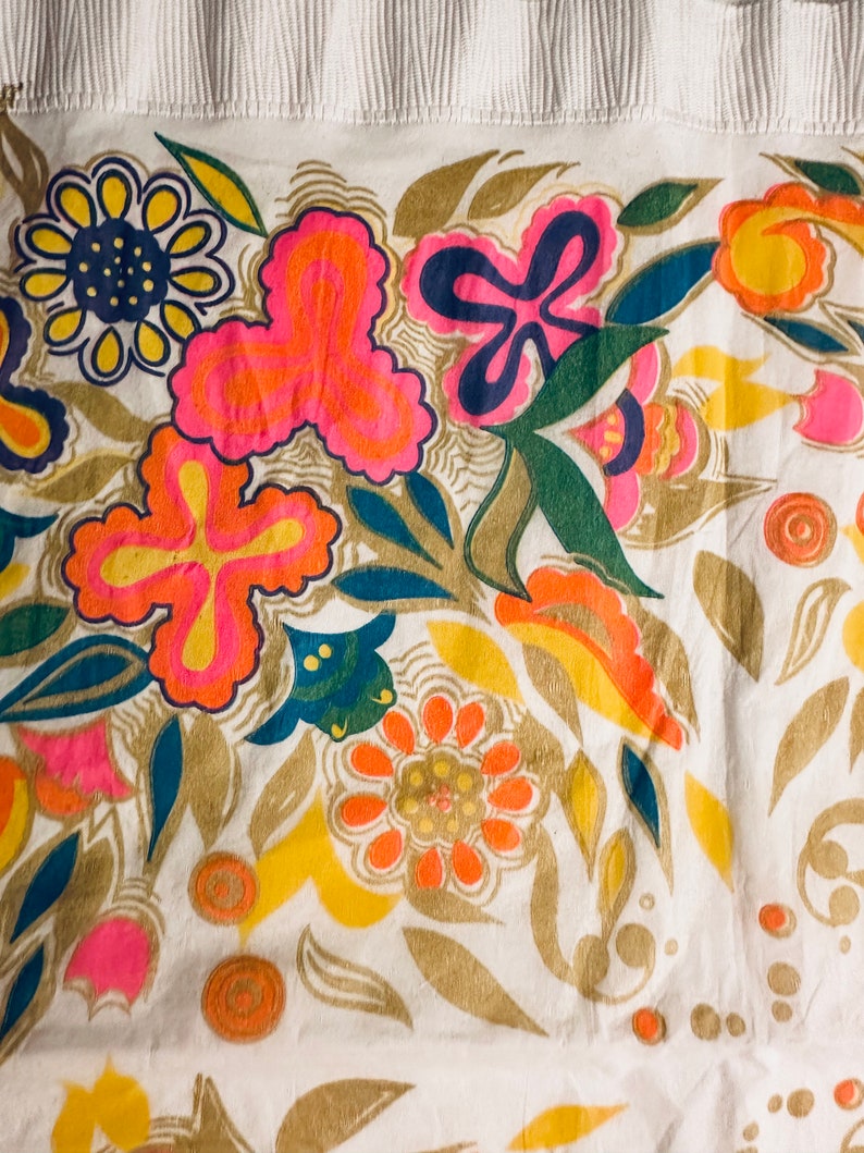 May include: A white fabric with a colorful floral pattern. The flowers are in shades of pink, orange, yellow, blue, and green. The fabric has a textured surface.