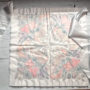 May include: A white satin ribbon with a floral pattern on a white background. The ribbon is tied in a bow and the ends are hanging down.