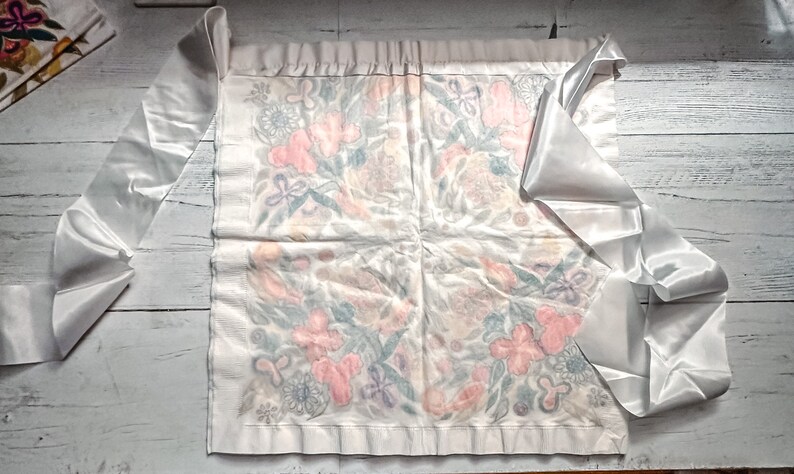 May include: A white satin ribbon with a floral pattern on a white background. The ribbon is tied in a bow and the ends are hanging down.