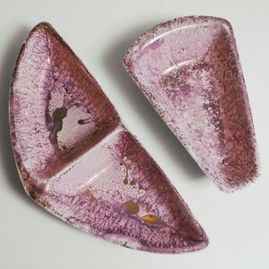 May include: Two ceramic serving dishes with a pink and brown speckled glaze. The larger dish has two sections, while the smaller dish is a single section.