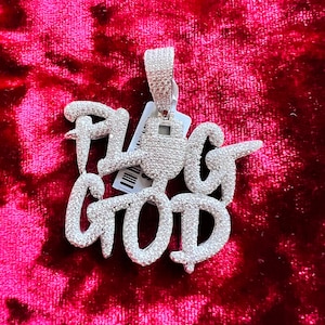May include: A silver pendant with the words "Plug God" set in sparkling white stones. The pendant is on a red velvet background.