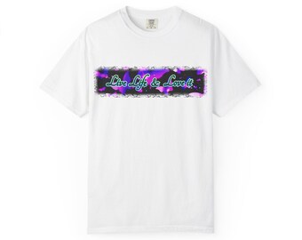 May include: White t-shirt with a graphic design. The design features the text "Live Life & Love It" in a teal font, set against a purple and black background with a floral border. The shirt is made of a soft material.