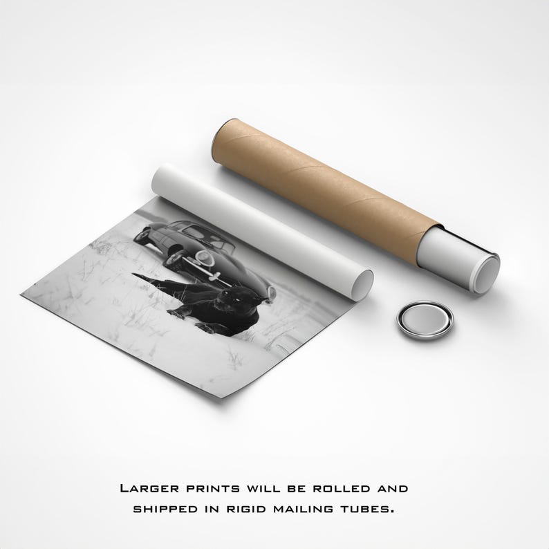 May include: Black and white print of a vintage car on a snowy landscape, next to a rolled-up poster and mailing tube. The print is partially unrolled, revealing the car's reflection. The text at the bottom reads: "LARGER PRINTS WILL BE ROLLED AND SHIPPED IN RIGID MAILING TUBES."