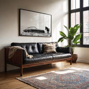 K&ouml;nnte beinhalten: Ein schwarzes Ledersofa mit Holzarmlehnen und -beinen steht in einem Wohnzimmer mit einem gro&szlig;en Fenster und einem Teppich. Ein Schwarzwei&szlig;foto eines Autos und eines Pferdes h&auml;ngt an der Wand &uuml;ber dem Sofa.