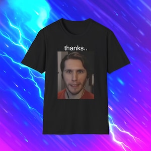 May include: A black short-sleeved t-shirt featuring a rectangular graphic print of a person with dark hair wearing an orange shirt. Above the image, the word thanks.. is printed in white lowercase letters against the black fabric background.