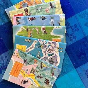 May include: A stack of vintage travel brochures with colorful maps and illustrations. The brochures feature destinations like "South Around the World", "The Queen", "The Federation of Rhodesia and Nyasaland", and "American Desert".