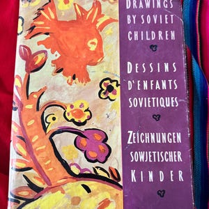 May include: A purple book with the title "Drawings by Soviet Children" in white text. The cover features a colorful illustration of a bird and flowers.