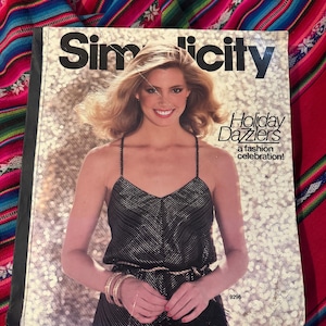 May include: A vintage Simplicity sewing pattern book titled "Holiday Dazzlers, a fashion celebration!" The cover features a smiling woman in a black sequined dress. The book is set against a sparkly background.