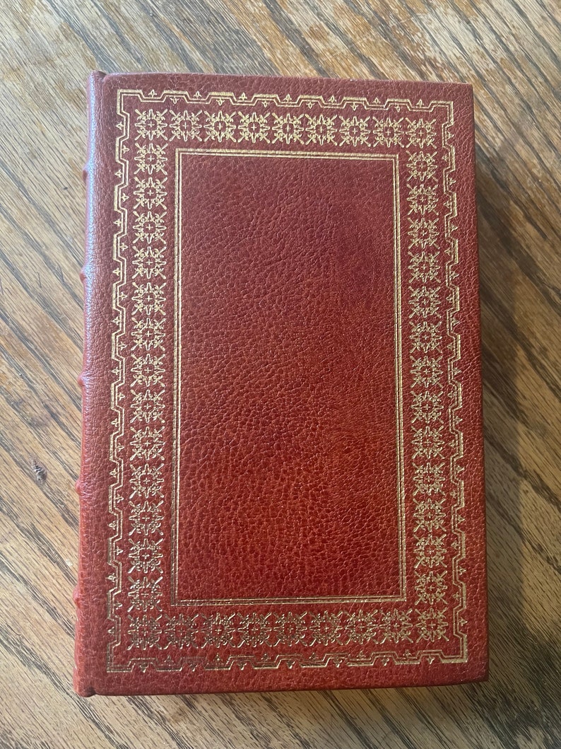 May include: A brown leather-bound book with a gold-coloured decorative border around the cover.