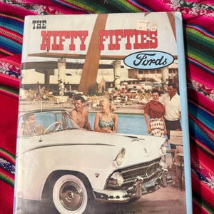 May include: A vintage book titled "The Nifty Fifties Fords" with a white convertible car on the cover. The cover art depicts people in swimwear near a pool. The book's title is in red letters with a blue oval logo that says "Fords".
