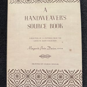 May include: A vintage book titled "A Handweaver's Source Book" with a cream-colored cover and brown geometric patterns. The book features text including the author's name, editor, and a selection of patterns from the Laura M. Allen collection.
