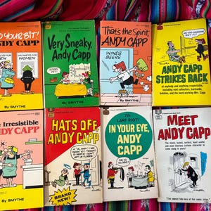 May include: A collection of vintage Andy Capp comic books. The covers feature colorful illustrations and text, with titles like "Very Sneaky, Andy Capp" and "Andy Capp Strikes Back." The books are arranged on a patterned textile.