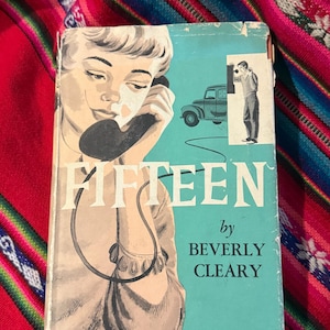 May include: Vintage book cover for "Fifteen" by Beverly Cleary. The cover features an illustration of a woman on the phone, a car, and a man. The title is in white, and the author's name is in black on a teal background.